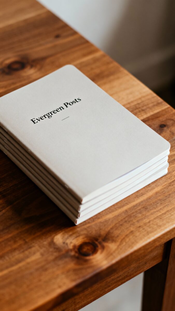 Stacked notebooks titled “Evergreen Posts” on wooden table